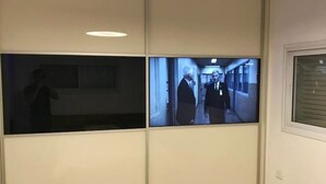 Une pièce dotée d’une porte coulissante, d’un luminaire au plafond et d’un écran de télévision qui diffuse une scène se déroulant dans un couloir.