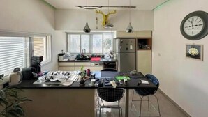 Une cuisine moderne dotée d’un îlot central, de luminaires suspendus et d’une horloge au mur.