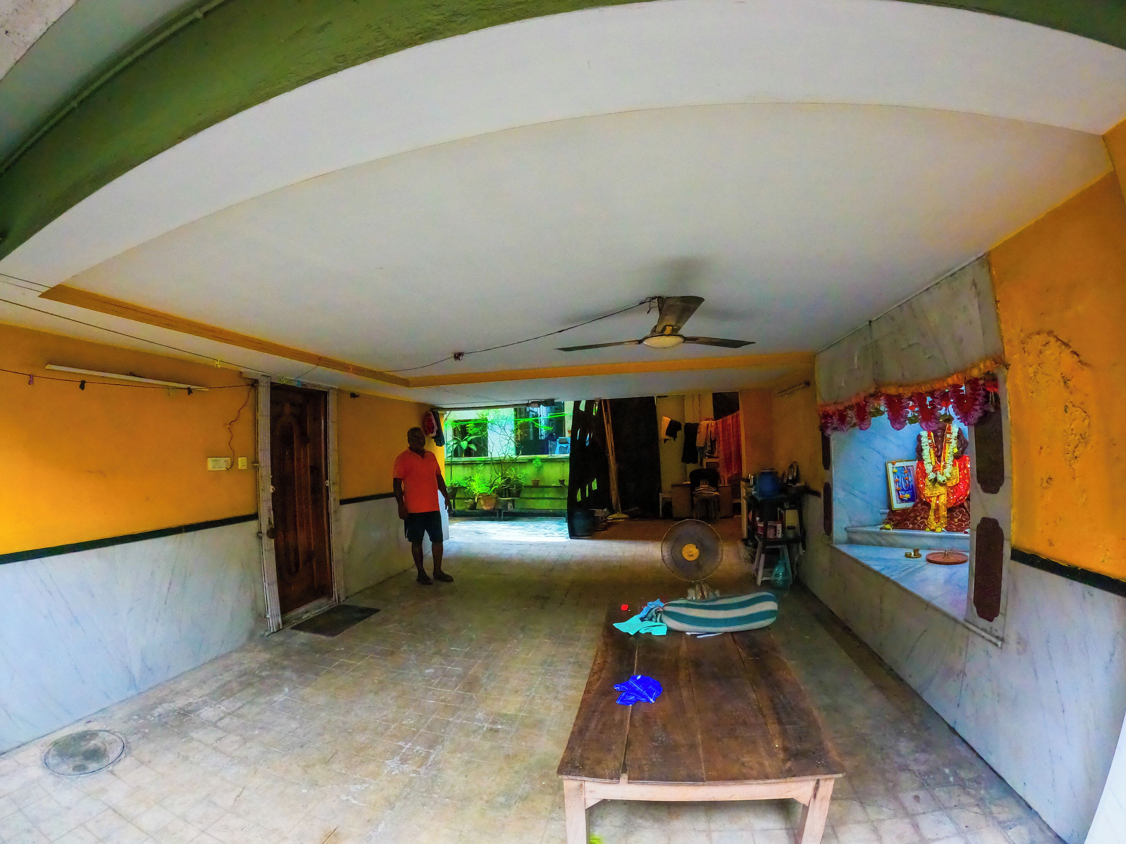 A room with a ceiling fan, a table with a blue object, and a shrine with flowers.