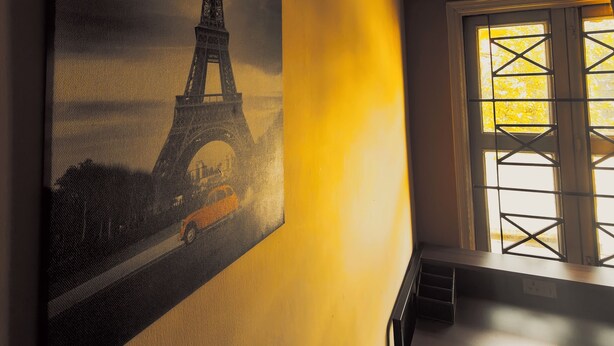 Una habitación con un cuadro grande de la Torre Eiffel, una ventana que da a árboles y un escritorio con una silla.