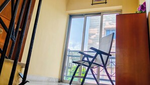 Una escalera con barandilla de madera, un ventilador de techo, una ventana con vista a edificios y una silla en el rellano.