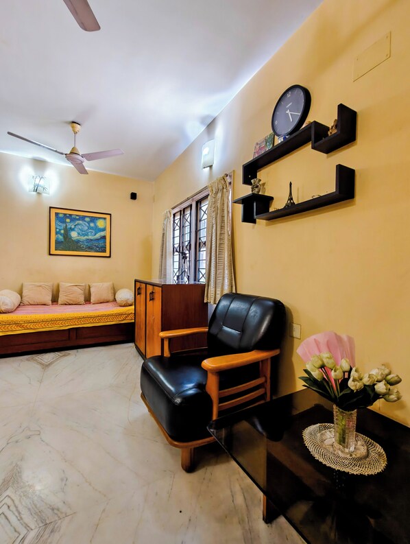 Una sala de estar con un sofá, un sillón de cuero negro, un reloj y un cuadro en la pared.