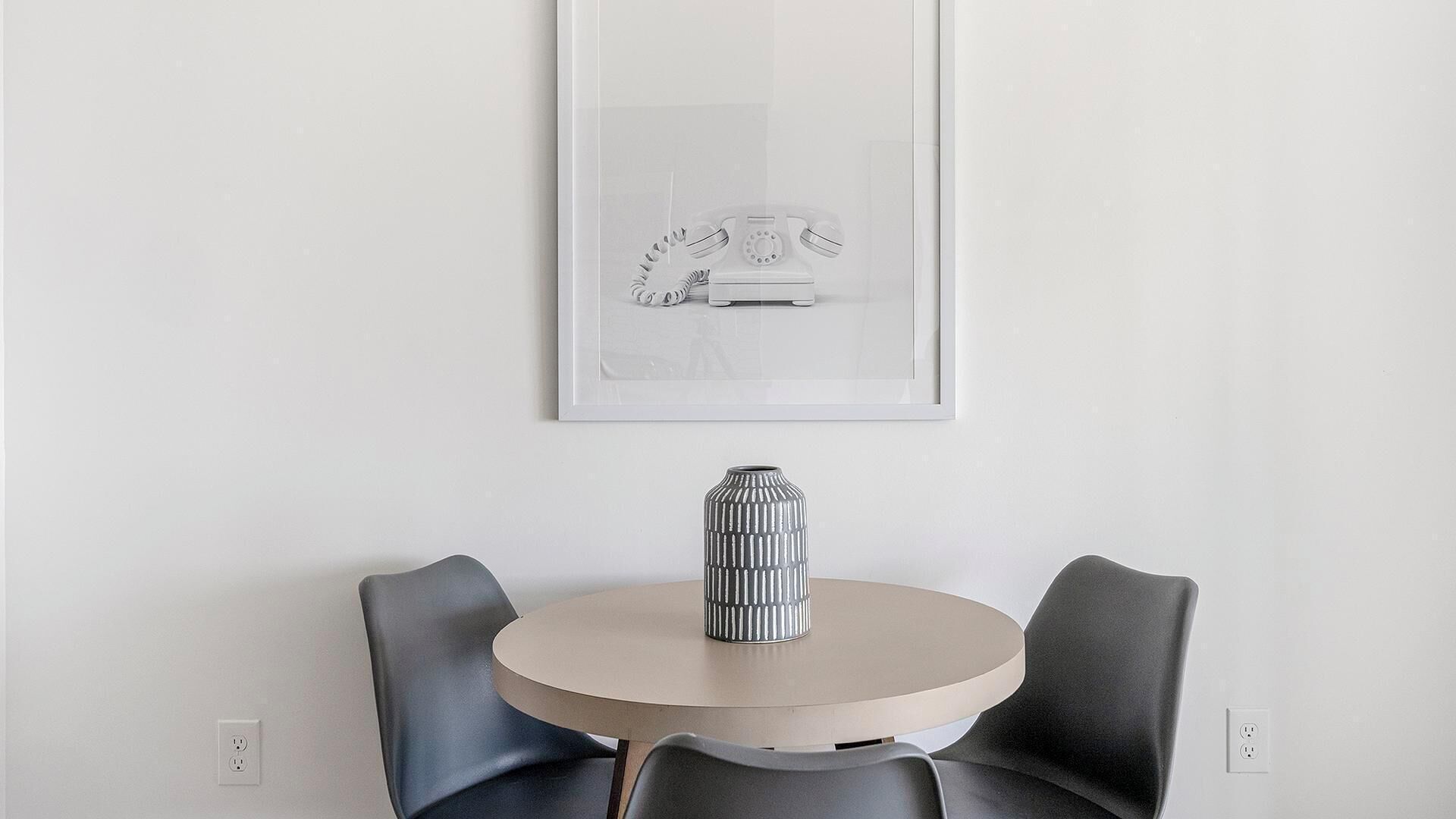 A round table with two chairs, a vase, and a framed picture on the wall.