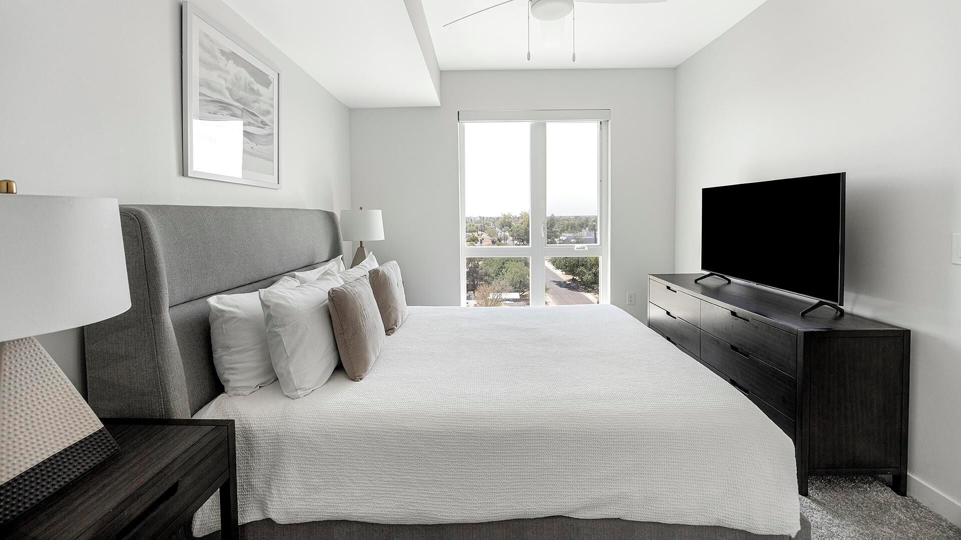 A modern bedroom with a large bed, a TV, and a view of the outdoors.