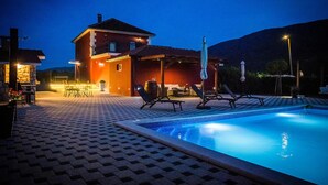 A pool area with lounge chairs, a covered seating area, and a building with a stone facade.