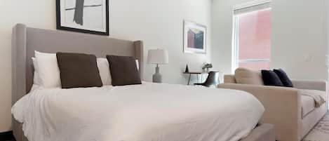 Et hotelværelse med en stor seng, en sofa, et skrivebord og et vindue med persienner.