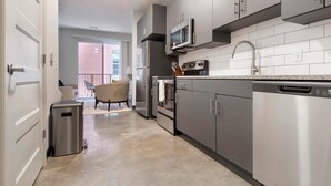 A modern kitchen with stainless steel appliances, grey cabinets, and a tiled backsplash. - Landing | Stunning Studio, Gym, Courtyard (St. Louis)