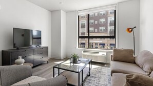 A modern living room with a flat-screen TV, a dark wooden cabinet, a glass coffee table, and a beige sofa. - Landing | Spectacular 1BD, Courtyard, Gym (New York)