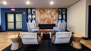 A lobby with a fireplace, two armchairs, a coffee table, and a wooden side table.