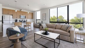 A modern living room with a sofa, coffee table, and a dining area with a kitchen in the background.