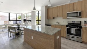 Een moderne keuken met houten kastjes, een granieten aanrechtblad, roestvrijstalen apparatuur en een eethoek met een tafel en stoelen.