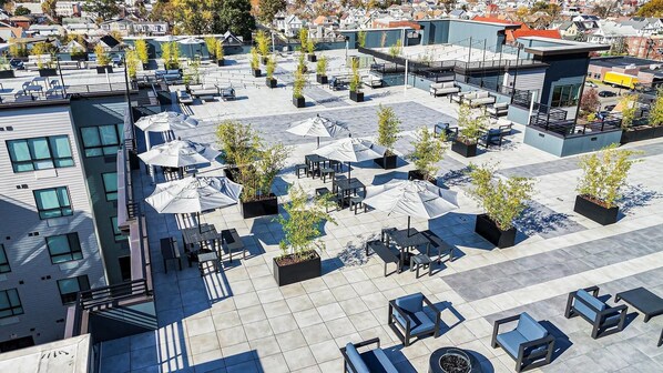 Un área de estar al aire libre con mesas y sombrillas, rodeada de edificios.