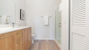 A modern bathroom with a wooden vanity, a glass shower enclosure, and a white toilet. - Landing | Beautiful 2BD, Game Room, Pool (Orlando)