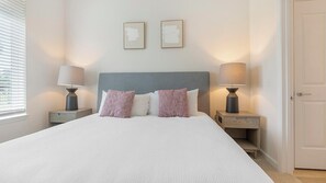 A neatly made bed with a grey headboard, two bedside lamps, and two framed pictures on the wall. - Landing | Beautiful 2BD, Game Room, Pool (Orlando)