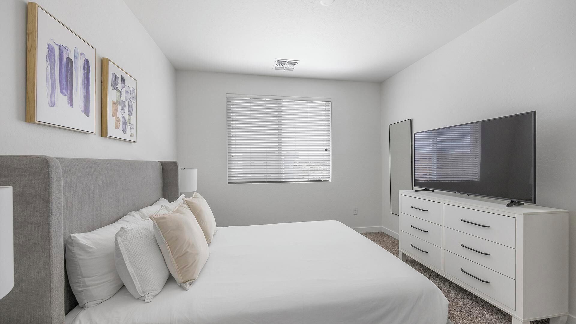 A bedroom with a bed, a TV, a dresser, and a window with blinds.