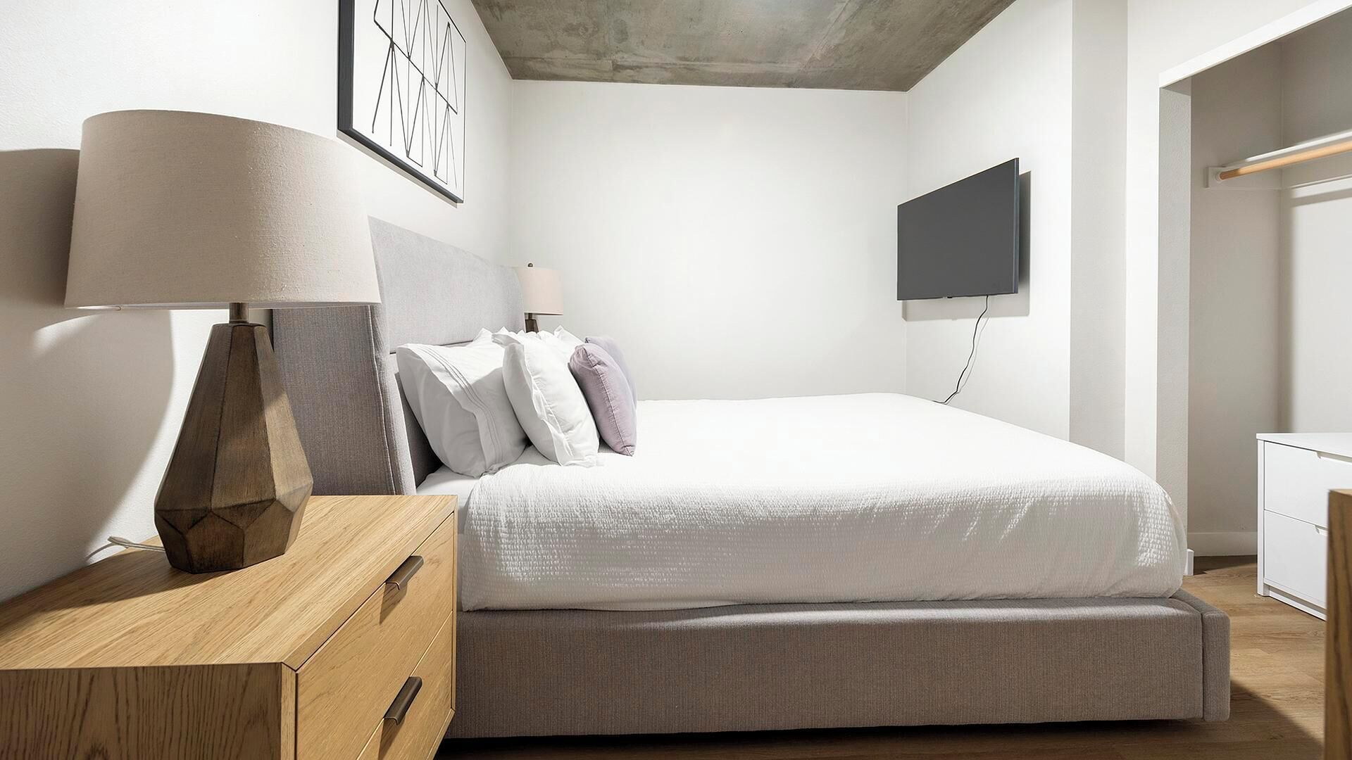 A modern bedroom with a bed, a bedside table, a lamp, a wall-mounted TV, and a wardrobe.