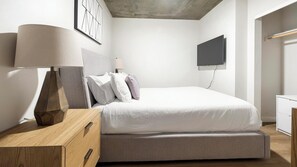 Et moderne soveværelse med seng, sengebord, lampe, fjernsyn på væggen og et garderobeskab.