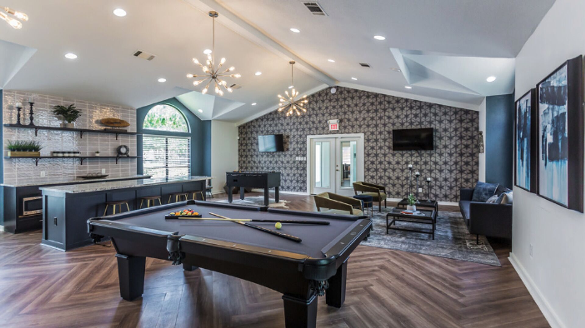 A modern indoor space with a pool table, bar area, and seating.