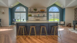 Een moderne keuken met een centraal eiland, barstoelen en grote ramen.