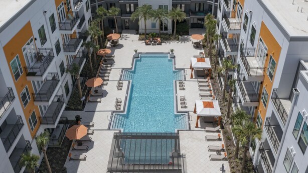 A rooftop pool area with multiple lounge chairs and umbrellas, surrounded by apartment buildings. - Landing | Stylish 2BD, Gym, Pool (Jacksonville)