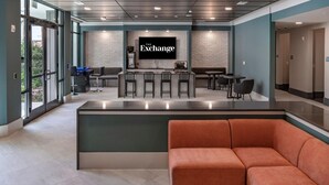 A modern interior with a bar area, seating, and a TV screen displaying 'The Exchange'.