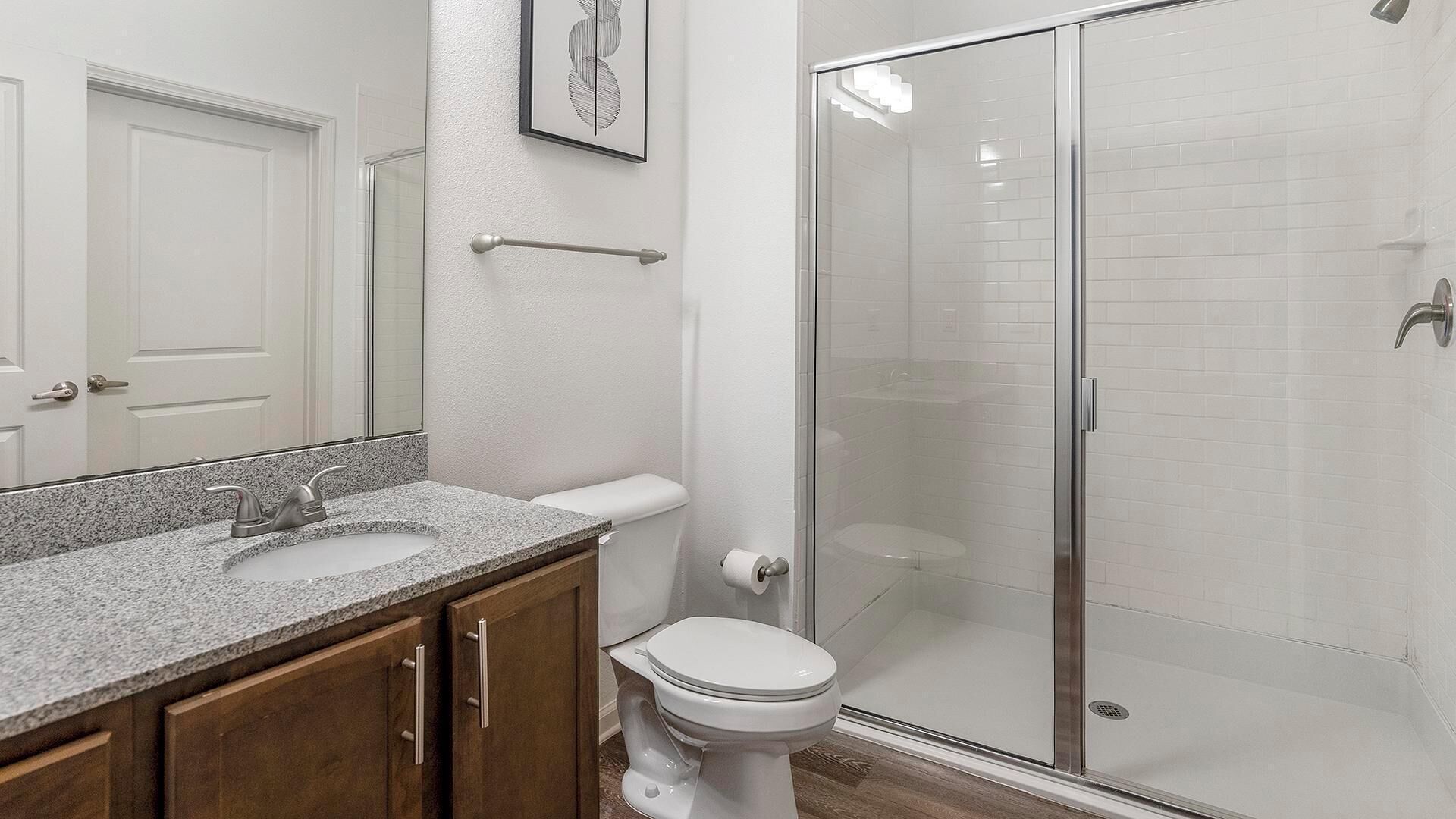 Un baño con lavamanos de encimera de granito, inodoro y ducha con mampara de vidrio.
