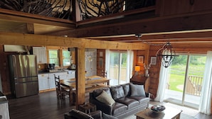 A spacious living area with a wooden ceiling, a dining table, a sofa, and a kitchen in the background.
