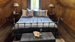 A cozy attic bedroom with a metal bed frame, a bedside table with a lamp, and a window with curtains.