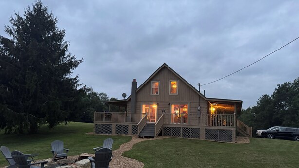 A two-story house with a deck, outdoor seating, and a fire pit.