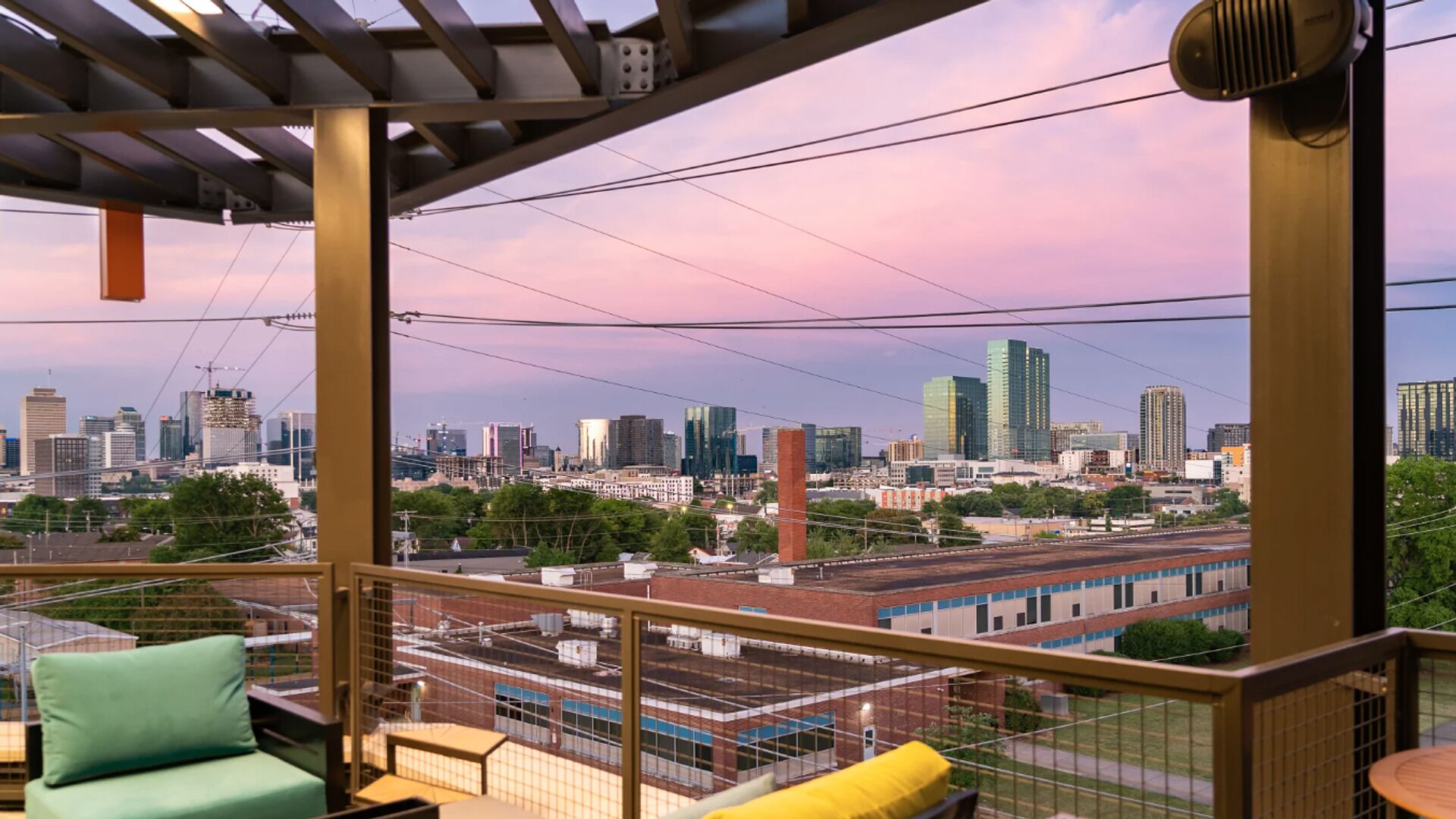 A balcony with a city view, featuring a metal railing, a green chair, and a yellow pillow.