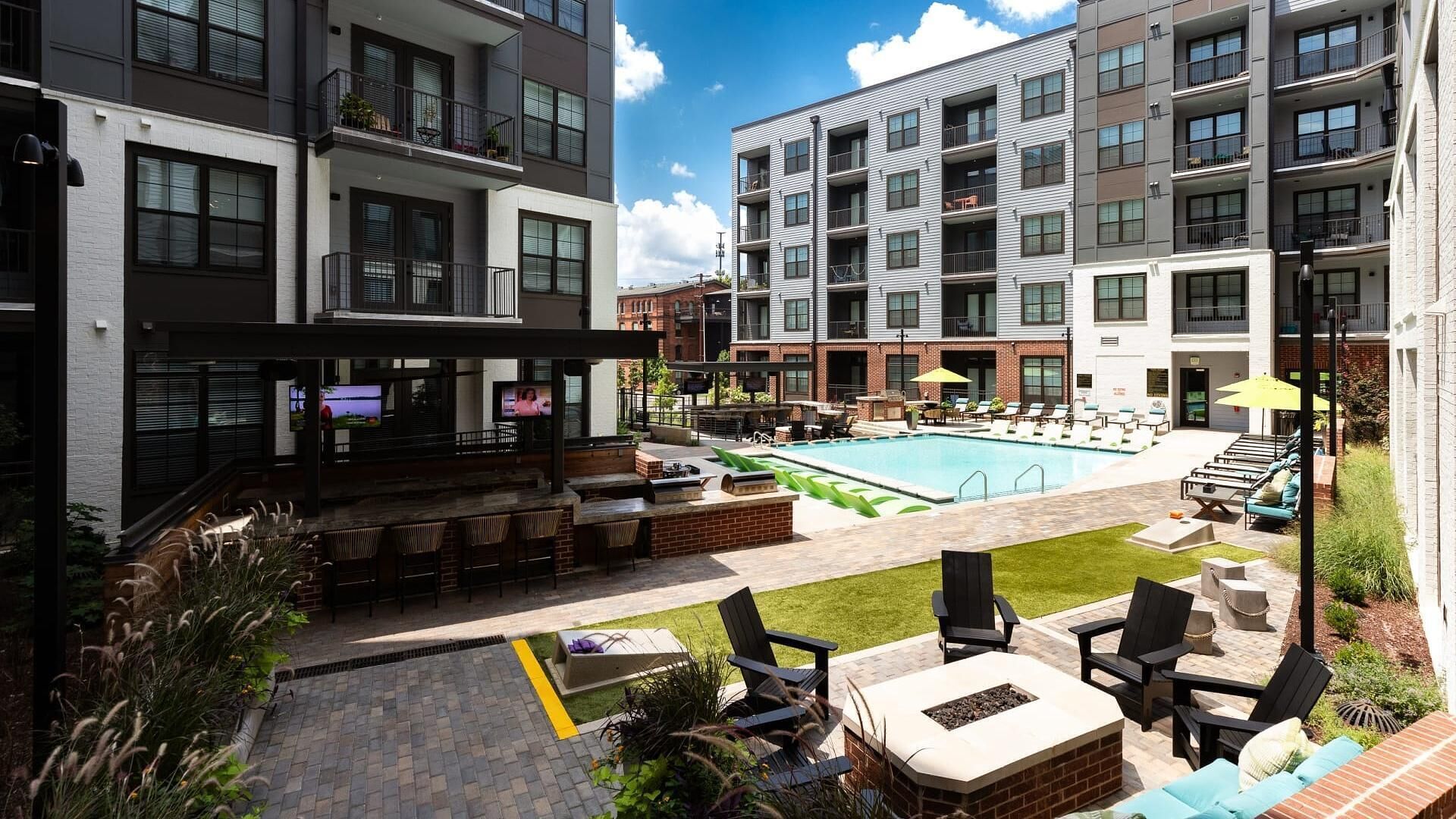 A modern apartment building with a rooftop pool, outdoor seating, and a bar area.