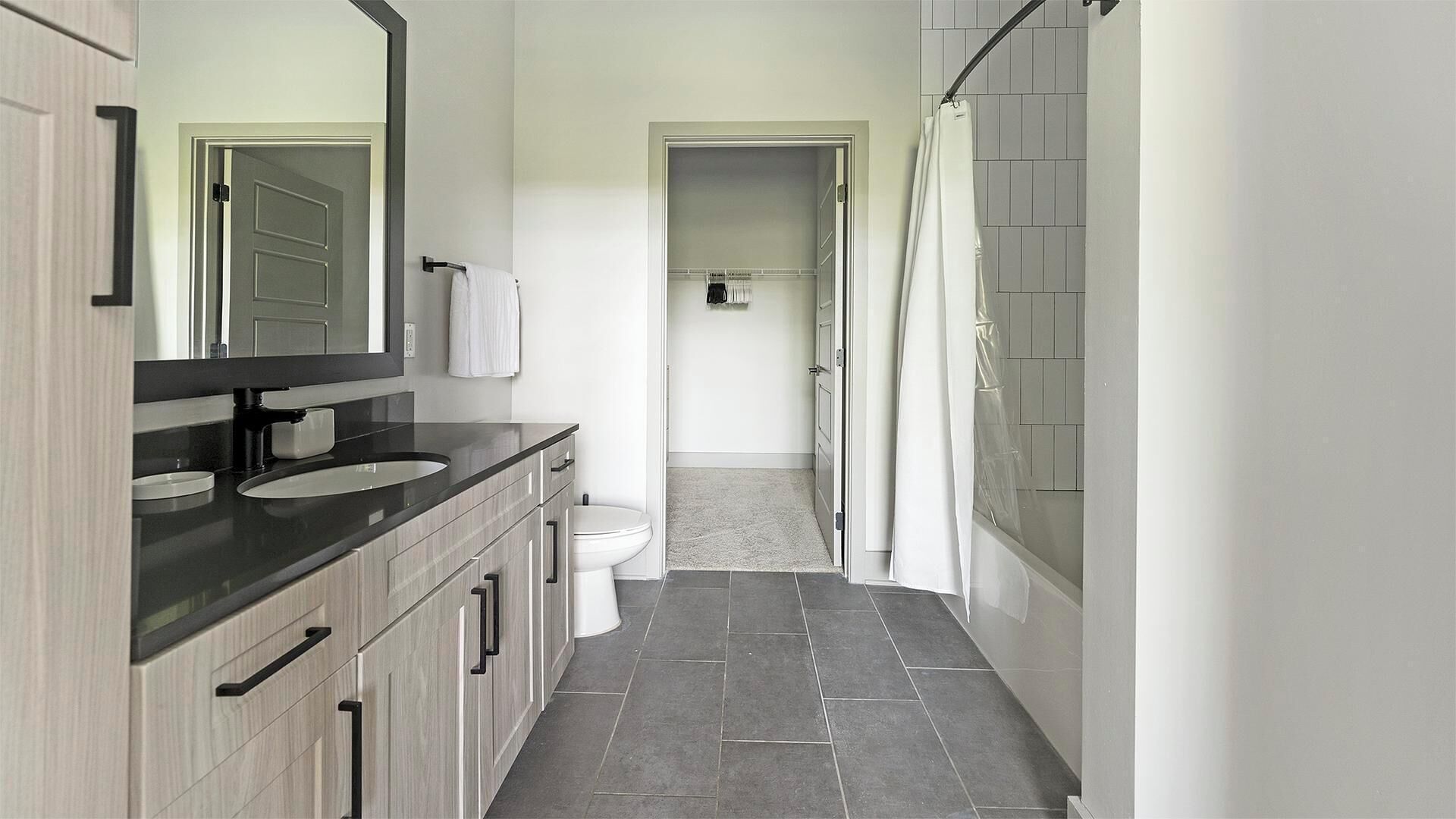 A modern bathroom with a dark countertop, two sinks, a toilet, and a shower area.