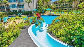 A resort pool area with a water slide, lounge chairs, and palm trees. - Partial Ocean View 1BR +Queen Sleeper Sofa, Prime Location 
Family Friendly (Kapaa)
