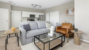 Una sala de estar moderna con un sofá gris, un sillón de cuero marrón y una mesa de centro de vidrio.