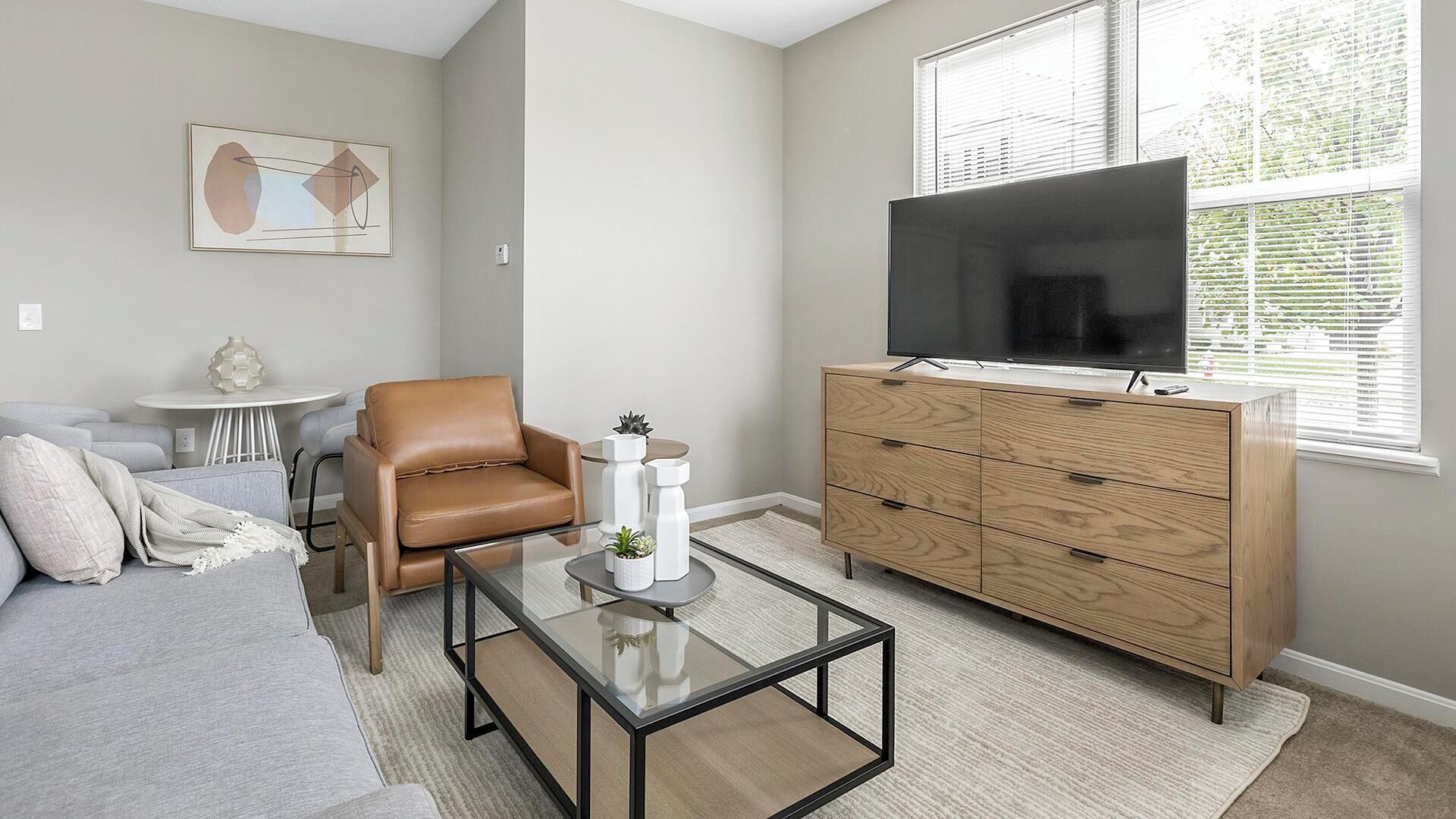 A modern living room with a leather armchair, a glass coffee table, a wooden dresser, and a flat-screen TV.
