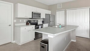 Una cocina moderna con armarios blancos, electrodomésticos de acero inoxidable y una isla central con lavamanos.