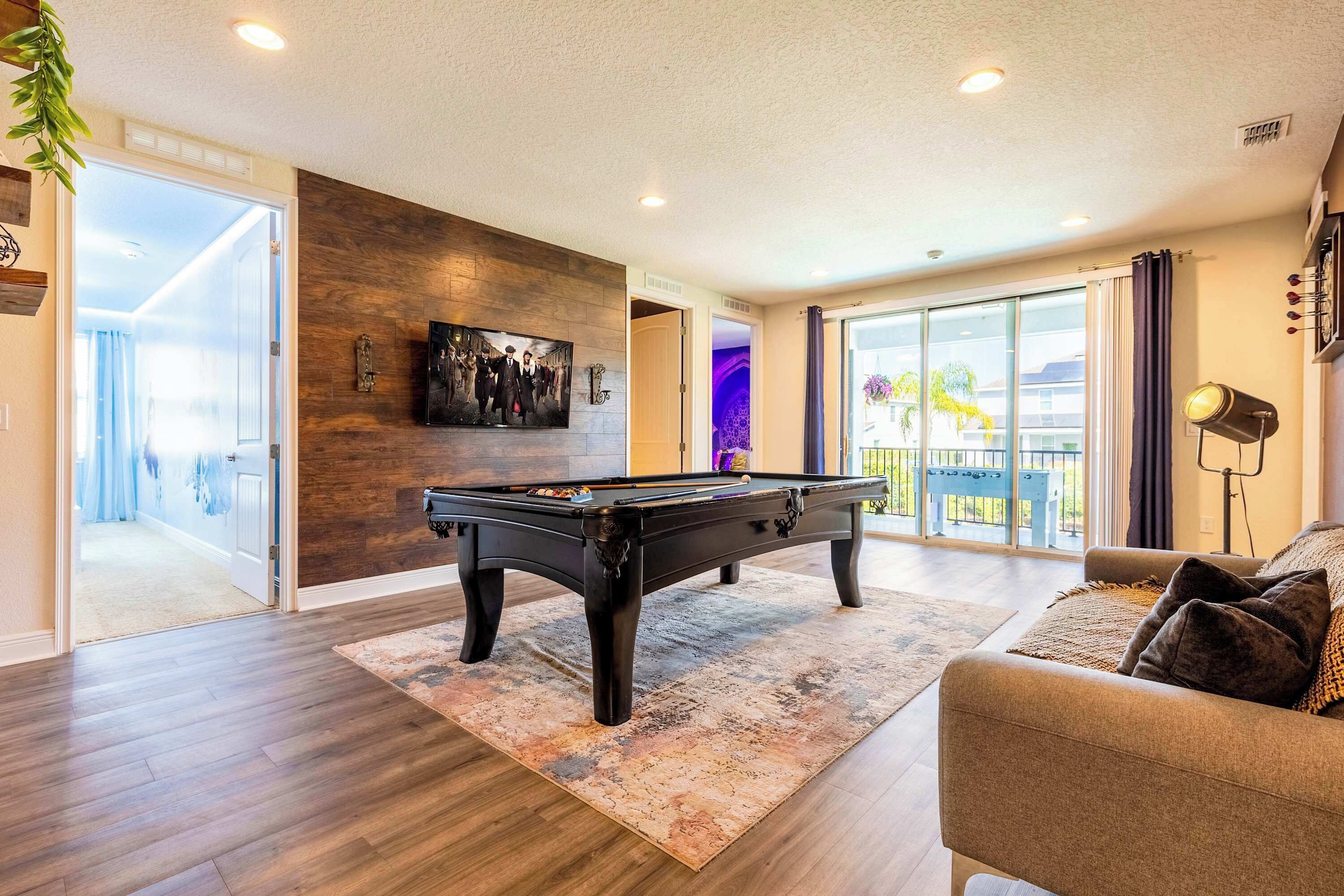 A modern living room with a pool table, a comfortable sofa, and a large window offering a view of the outdoors.