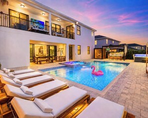 Une piscine avec des chaises longues, un flotteur en forme de flamant rose et un espace bar.