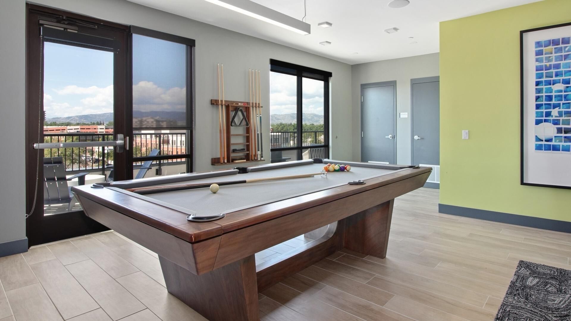 A pool table in a modern room with large windows, a balcony, and a view of the mountains.