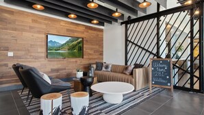 A modern lounge area with a wooden wall, a large framed landscape photo, a sofa, a coffee table, and a chalkboard sign. - Landing | Chic Studio in Fort Collins (Fort Collins)