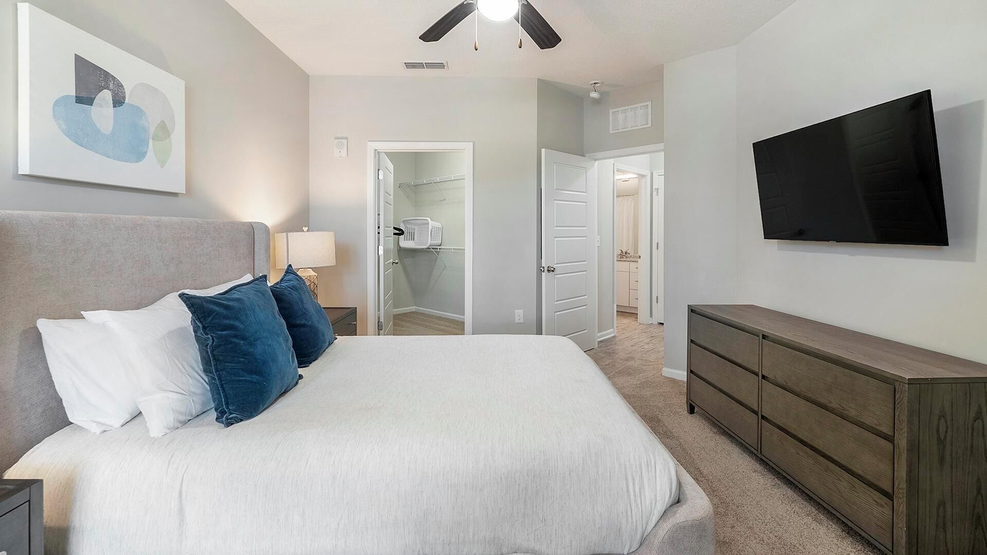 A bedroom with a bed, a TV, a ceiling fan, and a door leading to a bathroom.