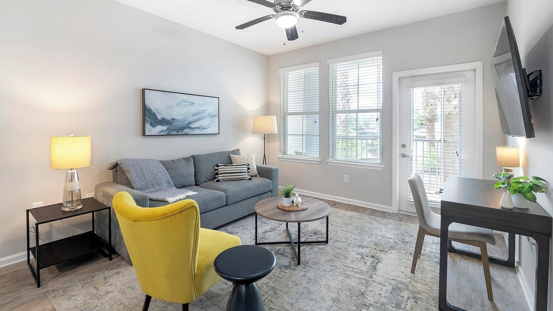A modern living room with a grey sofa, a yellow armchair, a coffee table, and a TV mounted on the wall.