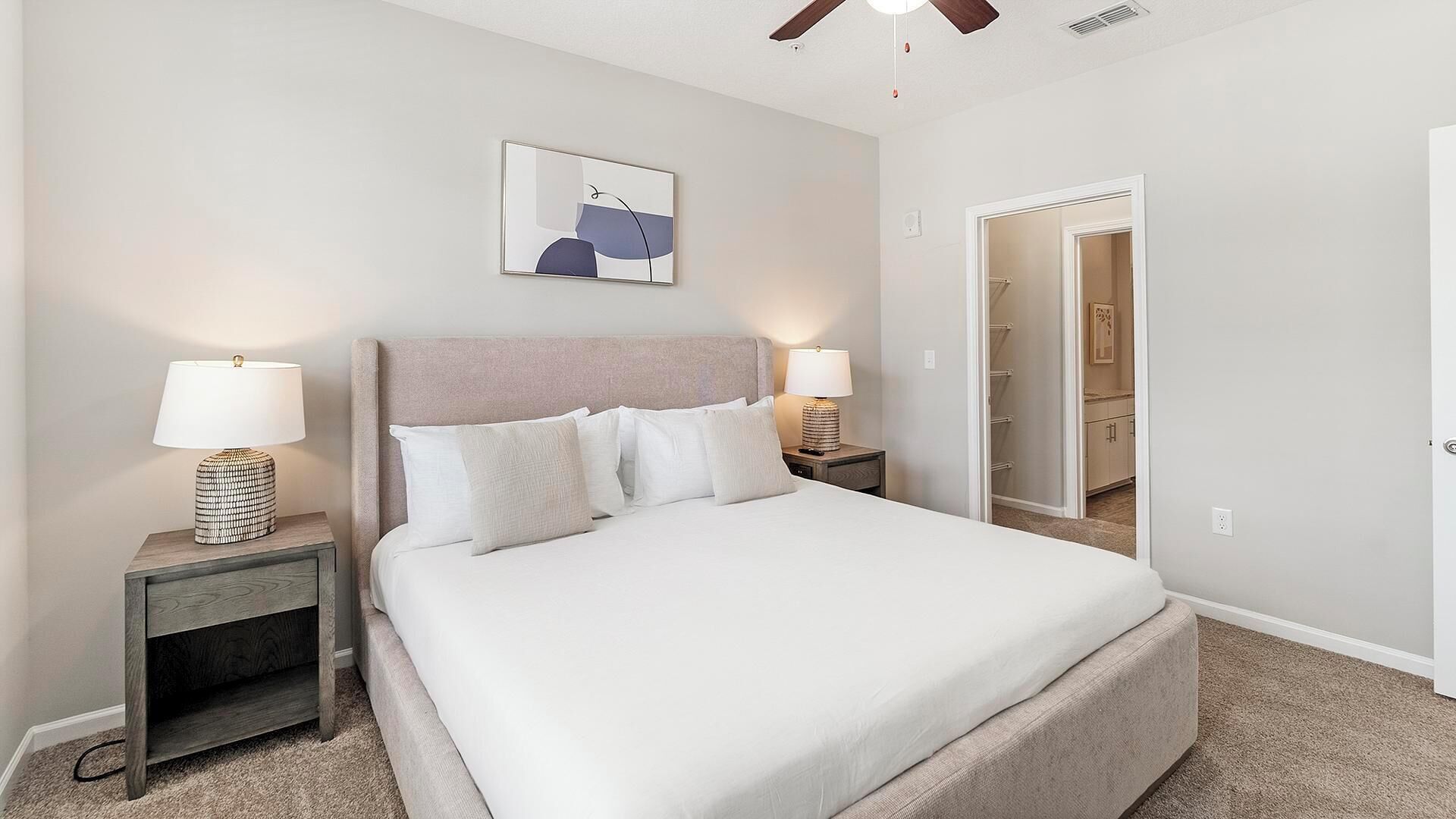 Una camera da letto ordinata con un letto grande, due comodini con lampade, una ventola a soffitto e una porta che dà su un bagno.