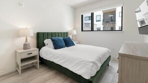 A modern bedroom with a green upholstered headboard, white bedding, and a nightstand with a lamp. - Landing | Amazing 1BD, Rooftop Lounge, Game Room (Richmond)