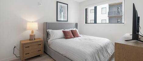 A modern bedroom with a bed, bedside table, lamp, and a TV.
