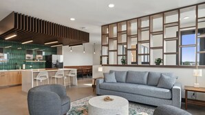 Een moderne woonkamer met een grijze bank, een ronde salontafel, en een eethoek met een groene spatwand en witte stoelen.