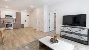 Een moderne keuken met een magnetron, oven en kastjes. Er is een eethoek met een tafel en stoelen, en een tv op een standaard.