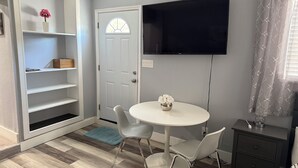 A compact room with a white door, a mounted TV, a round table with two chairs, and a small bedside table with a lamp. - Stay in style and comfort (central location) (Tampa)