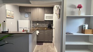 A modern kitchen with grey cabinets, a white refrigerator, and a microwave. There's a clock on the wall and a vase with flowers on the counter. - Stay in style and comfort (central location) (Tampa)