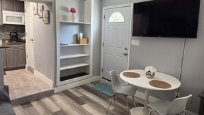 A modern kitchen with grey cabinets, a built-in microwave, and a coffee maker. There is a white dining area with a table and chairs, and a TV mounted on the wall. - Stay in style and comfort (central location) (Tampa)